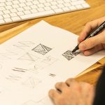 Designer's hand sketching logo ideas with a pen on paper next to a keyboard