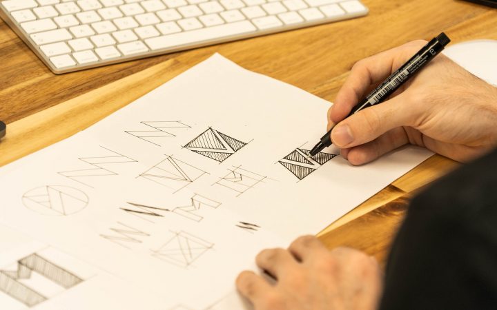 Designer's hand sketching logo ideas with a pen on paper next to a keyboard