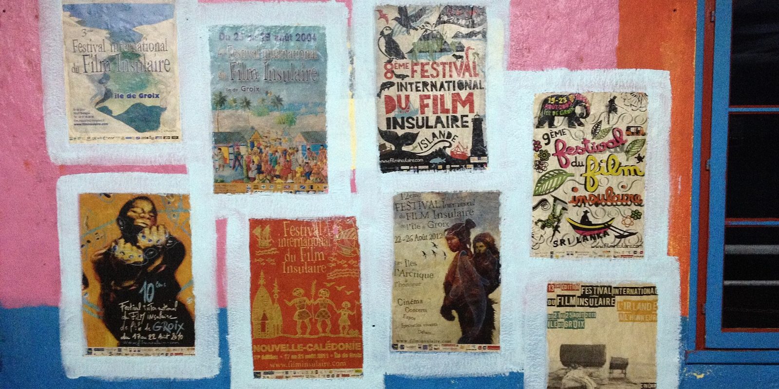 Colourful festival posters pasted on a brightly painted pink and blue wall