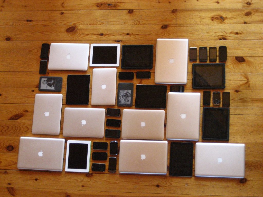 Laptops, tablets and smartphones laid out in a grid on a wooden floor