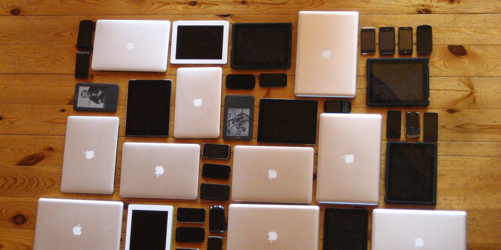 Laptops, tablets and smartphones laid out in a grid on a wooden floor