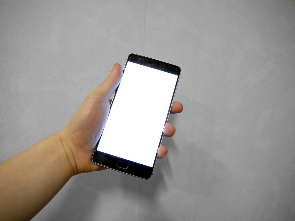 Hand holding a smartphone with a blank white screen against a grey background