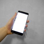 Hand holding a smartphone with a blank white screen against a grey background