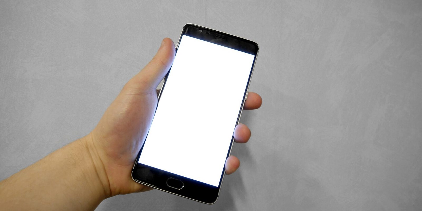 Hand holding a smartphone with a blank white screen against a grey background
