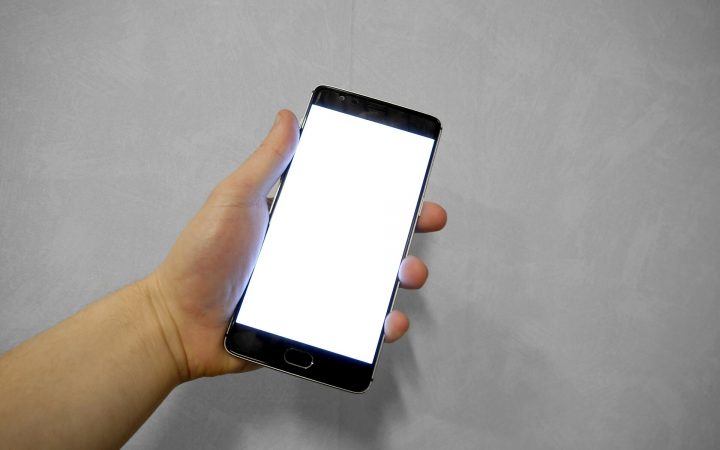 Hand holding a smartphone with a blank white screen against a grey background