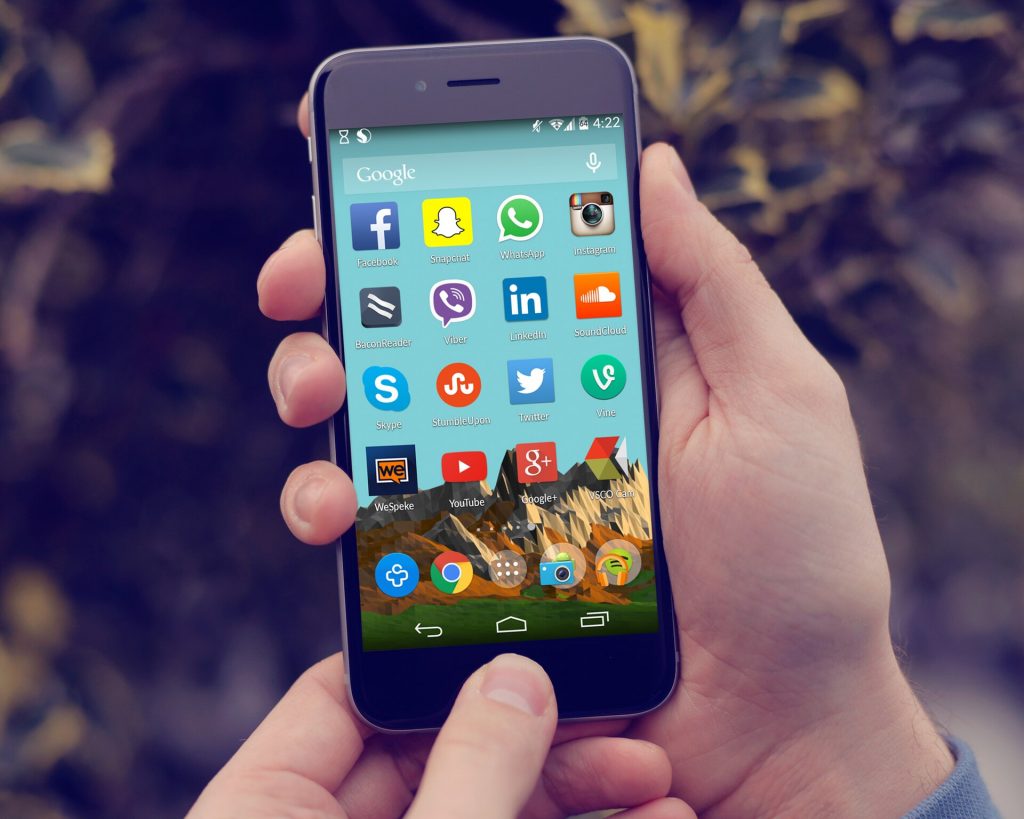 Hand holding an Android smartphone showing social media app icons on the home screen