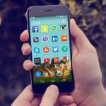 Hand holding an Android smartphone showing social media app icons on the home screen