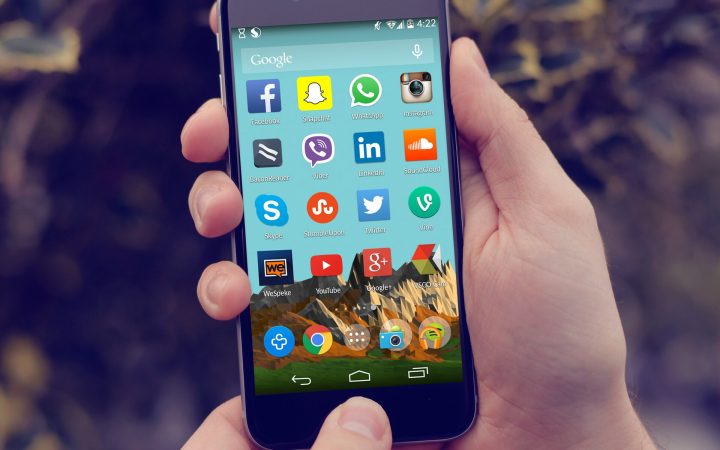 Hand holding an Android smartphone showing social media app icons on the home screen