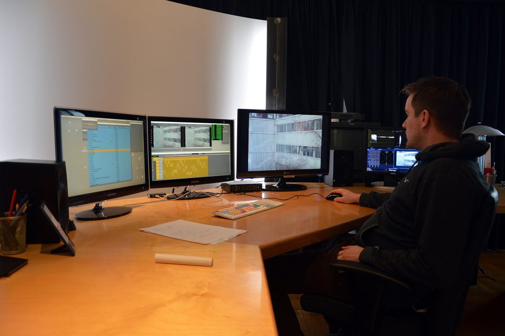 Editor at a digital editing suite with several monitors showing video editing software