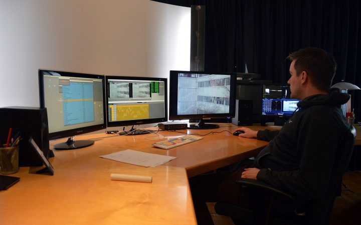 Editor at a digital editing suite with several monitors showing video editing software